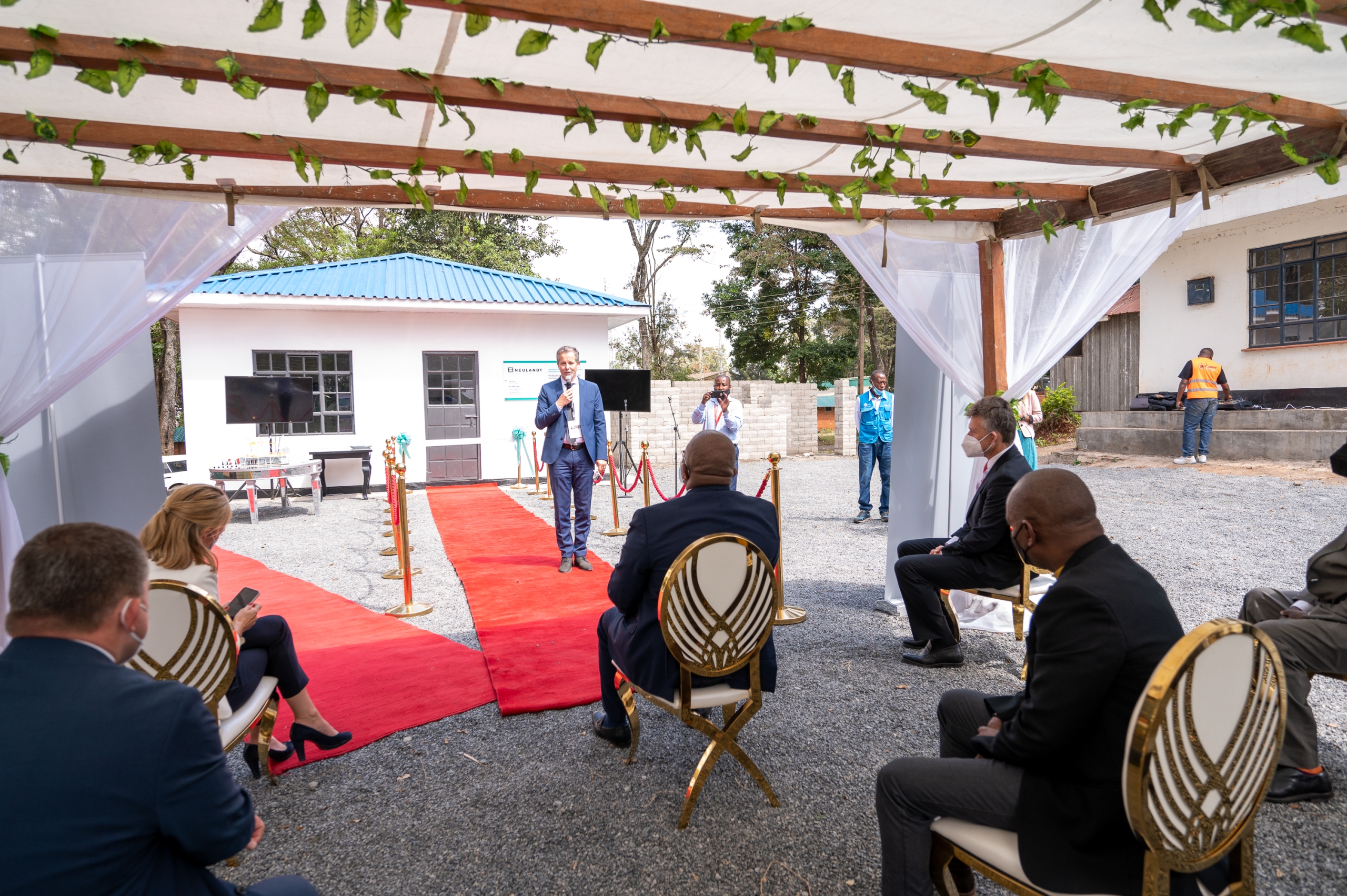 Crowd of business people is sitting on chairs under a pavilion while they are watching a business man giving a speech on the red carpet right in front of the show house at the NCA show ground in Kenia